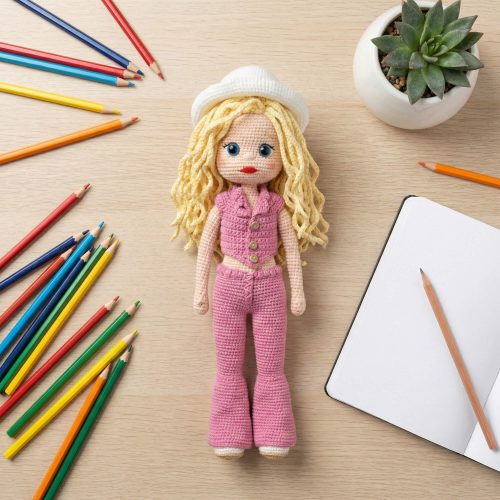 Ahşap masa üzerinde boya kalemleri ve defter ile birlikte sunulan sarı saçlı şık amigurumi bebek (Flat lay fotoğrafı).