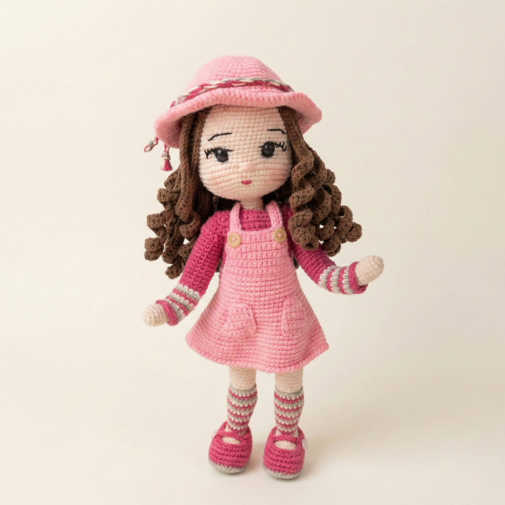 Pembe şapkalı, tulumlu ve kıvırcık saçlı el yapımı amigurumi bebek - önden tam boy görünüm.